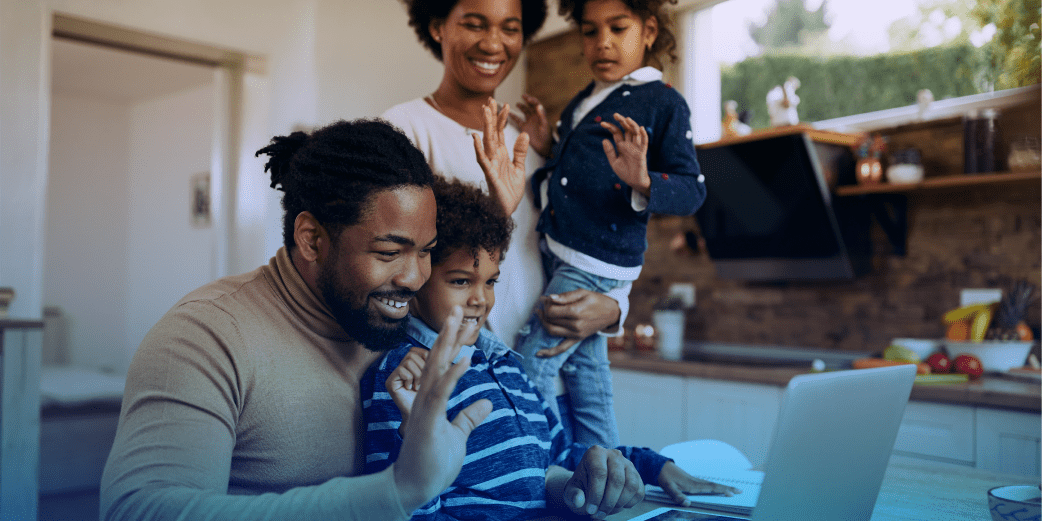 A family with two children gathered around a laptop in their kitchen